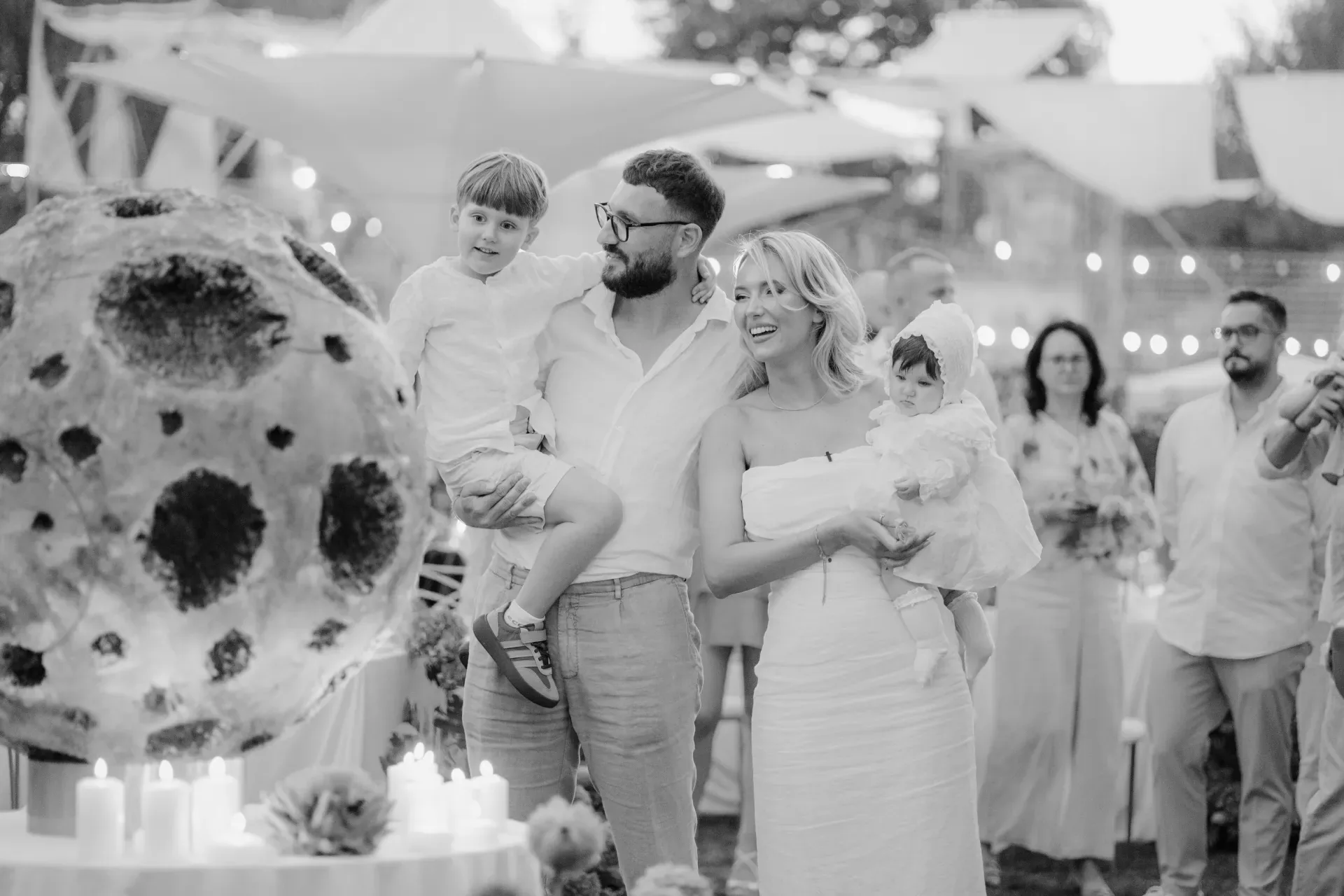 Fotograf botez Cluj-Napoca — familie în alb lângă sculptura lunii și lumânări, seara, moment editorial alb-negru