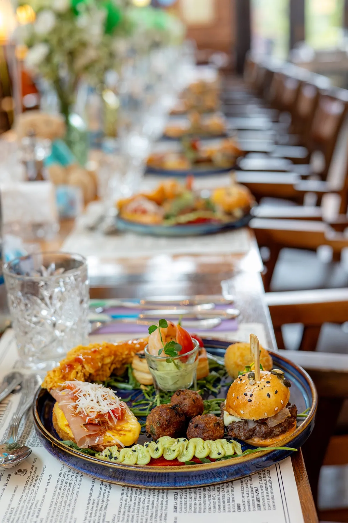 Platou de aperitive servit la masa lungă dintr-un restaurant de botez din Cluj-Napoca, cu burger, chiftele și creveți