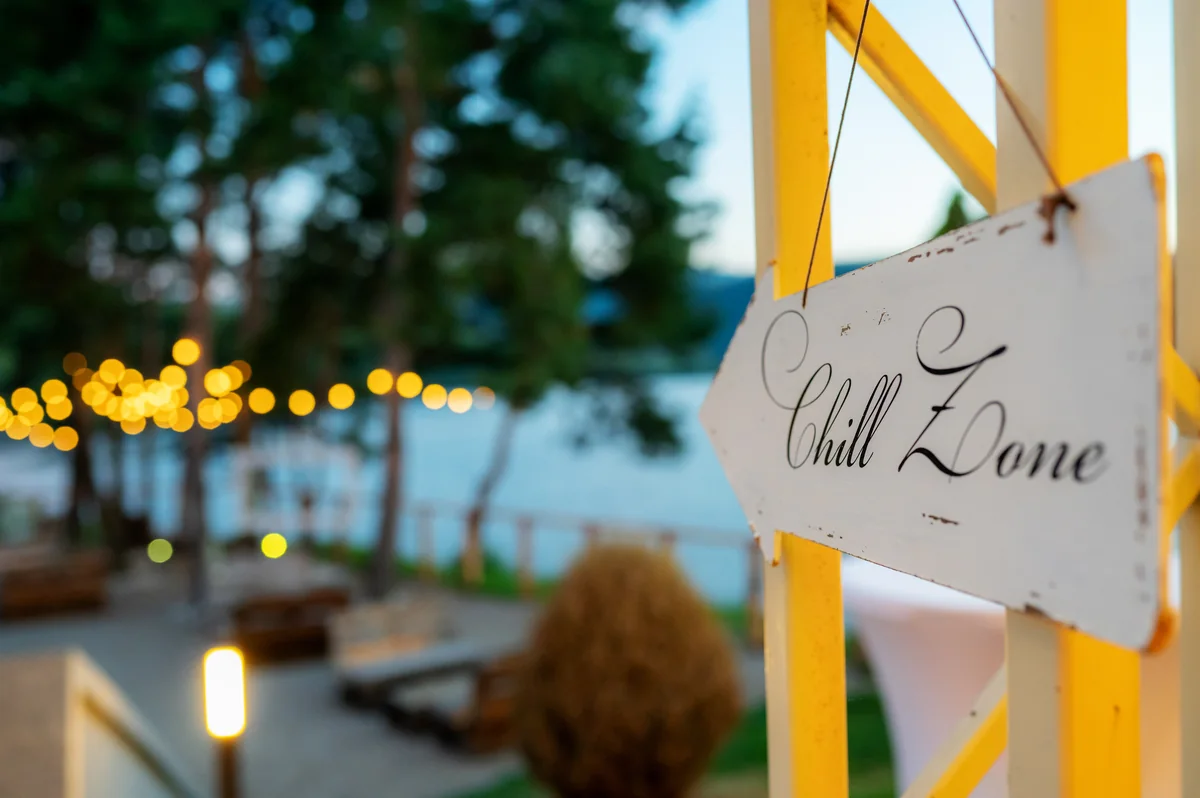 Indicator Chill Zone pe o structură galbenă la Motel Gilău, cu lacul și ghirlande de lumini în fundal, seara