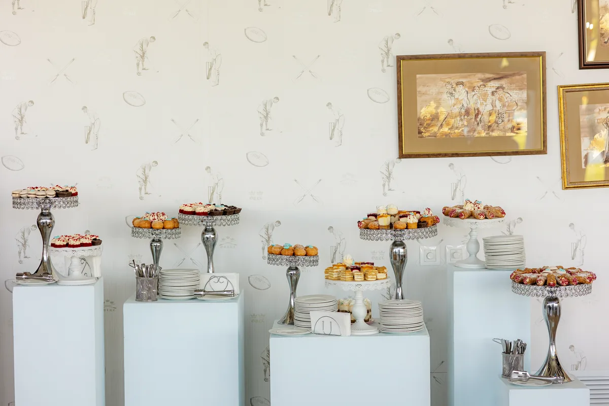 Candy bar elegant la un botez — prăjituri și macarons pe suporturi argintii, la înălțimi diferite — parte din costul petrecerii