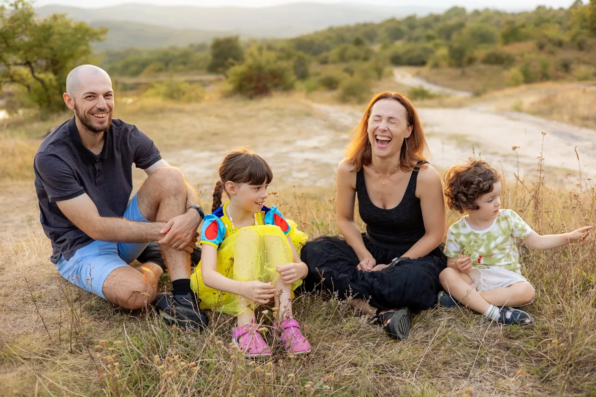 Familie râzând așezată în iarbă la o ședință foto de familie de vară, lângă Cluj-Napoca